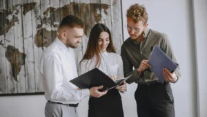 a group of young professional comparing notes in front of a distressed wooden world map